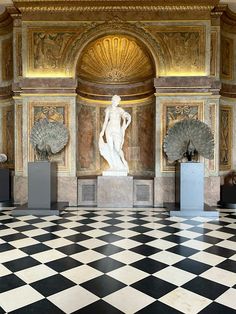 statues in the middle of a checkered floor with gold and white walls behind them