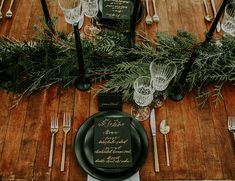 the table is set with black plates and silverware, greenery, and menus