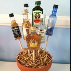 an arrangement of liquor bottles in a pot with straw shavings on the table