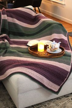 a blanket on a couch with a tea cup and candle sitting on top of it