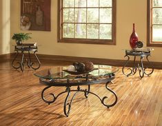 two tables with glass top sitting on wooden flooring in front of windows and vase