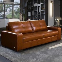 a brown leather couch sitting in a living room next to a lamp and bookshelf