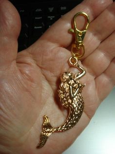 a hand holding a gold colored key chain with a mermaid on it's side