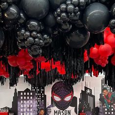 balloons are hanging from the ceiling in front of a spiderman themed party backdrop with black and red balloons