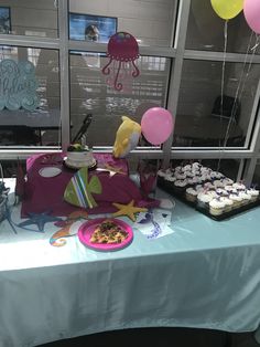 a table topped with cupcakes and cake next to windows filled with balloons in the shape of animals