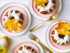 three plates topped with cakes and flowers on top of a white tablecloth next to gold forks