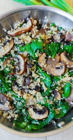 a pan filled with mushrooms and spinach on top of a wooden table next to green onions