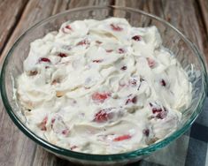 a glass bowl filled with cream cheese and strawberries on top of a wooden table