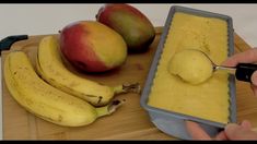 a person is dipping some fruit into a bowl on a cutting board with bananas and mangoes