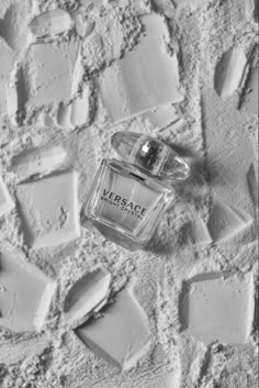 a bottle of perfume sitting on top of a white wall covered in ice cubes