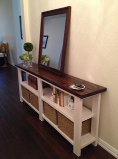 a white console table with two baskets under it and a mirror on the wall above it