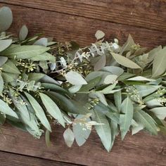 eucalyptus leaves and other greenery are laid out on a wooden surface, ready to be used as a garland