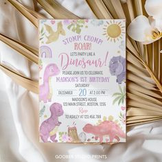 a pink dinosaur birthday party card on top of a white sheet with flowers and bamboo sticks