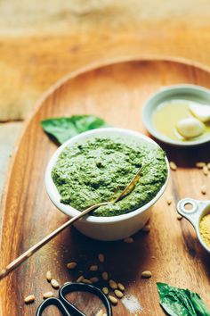 a wooden tray topped with bowls filled with green food next to scissors and spoons