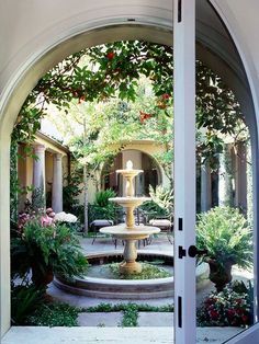 an open door leading to a courtyard with a fountain in the center and potted plants on either side