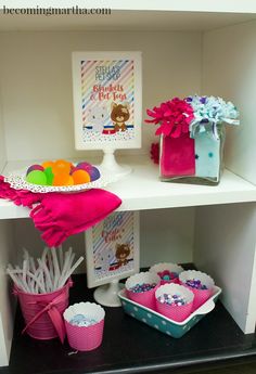 a shelf filled with lots of items on top of a white table next to cupcakes