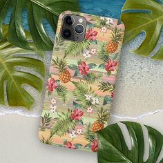 an iphone case with tropical flowers and pineapples on the beach next to palm leaves