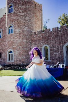 a woman with purple hair wearing a blue and white dress in front of a brick building