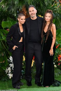 three people standing next to each other in front of plants and flowers at an event