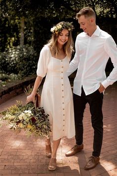 a man and woman walking down a brick walkway holding hands with each other while wearing white dresses