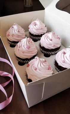 six cupcakes with pink frosting in a white box on a wooden table