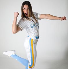 a woman is jumping in the air with her arms out and one leg up, wearing a baseball uniform