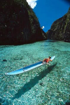 a person in a canoe paddling through the water near mountains and cliffs on a sunny day