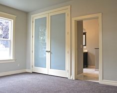 an empty room with two doors and carpeted flooring in front of the window