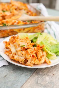 a white plate topped with pasta and lettuce next to a casserole dish