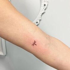 a woman's arm with a small dragonfly tattoo on the left inner arm