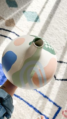 a hand holding a colorful vase on top of a rug