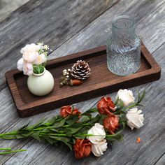 flowers and pine cones on a wooden tray next to a glass vase with water in it