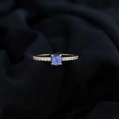 a tan gold ring with an oval blue stone surrounded by small white diamonds on a black cloth