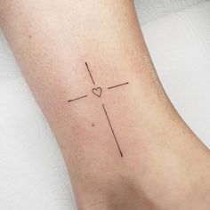 a small cross tattoo on the ankle with a heart at the top and an arrow at the bottom