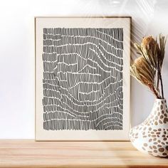 a vase with some dried flowers in it next to a framed art print on a shelf