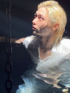 a man with blonde hair is floating in the water wearing a white shirt and necklace