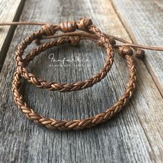 two braided leather bracelets sitting on top of a wooden table