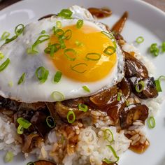 an egg on top of rice with mushrooms and scallions in the foreground