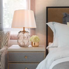 a nightstand with a lamp and flowers on it next to a bed in a bedroom