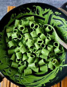 a pan filled with green pasta on top of a wooden table