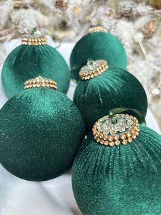 four green ornaments are sitting on a white cloth with gold trimmings and beading