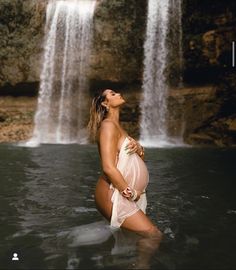 a pregnant woman standing in the water next to a waterfall