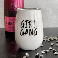 a wine glass with the word girl gang painted on it next to a bottle of wine