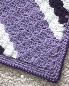 a purple and white crocheted blanket laying on top of a floor next to a rug