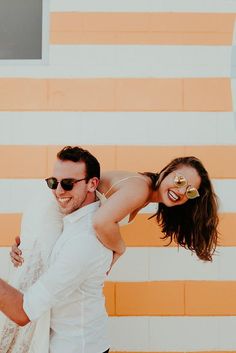 a man carrying a woman on his back in front of an orange and white wall