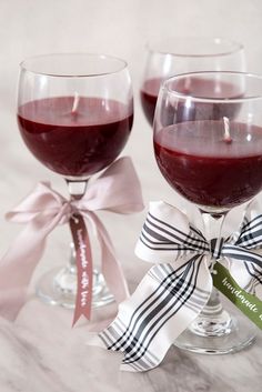 two wine glasses with red wine in them and ribbons tied around the rims, sitting next to each other