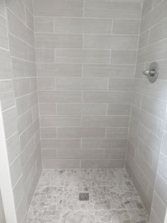 a walk in shower sitting next to a white wall and floor covered in gray tile