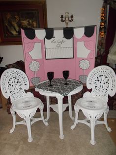 two white chairs and a table with wine glasses on it