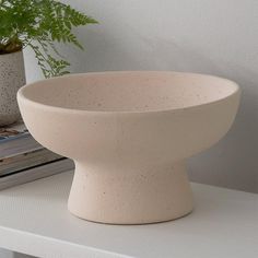 a large white bowl sitting on top of a table next to a potted plant