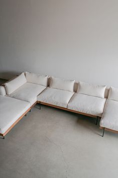 a white sectional couch sitting on top of a cement floor next to a wooden frame